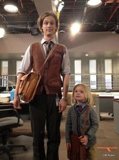 a young boy and girl standing next to each other in an office setting with lights on the ceiling