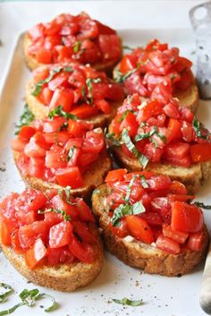 several pieces of bread topped with tomatoes and parsley on a white plate next to a knife