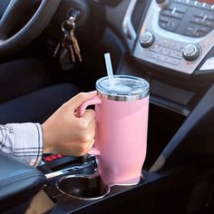 a person holding a pink cup with a straw in their hand while sitting in a car