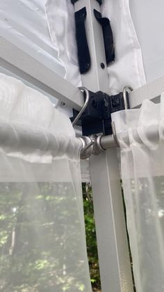 an open window with white curtains and black hardware on the bottom curtain is visible from outside