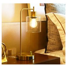 a lamp that is on top of a night stand next to a pillow and pillows