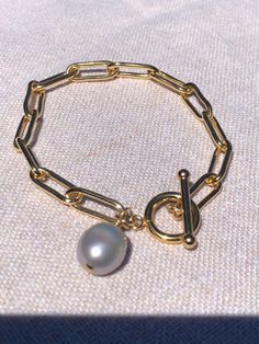 "Our best selling Classic large paperclip link chain bracelet in 14kt gold filled. Timeless toggle closure and a wire wrapped natural light grey pearl charm make this bracelet a stylish and classic piece to enjoy for years to come. Bracelet measures 7.5\" Includes Bracelet Helper gift with purchase! (See pictures) Price will vary for longer lengths.  Hand made in USA with 14Kt Gold filled materials made in USA 🇺🇸" Elegant Charm Bracelet With Toggle Clasp, Elegant Charm Bracelet With Toggle Clasp As Gift, Bracelet Helper, Pearl Charm Bracelet, Link Chain Bracelet, Toggle Bracelet, Gift With Purchase, Pearl Charms, Pearl Grey