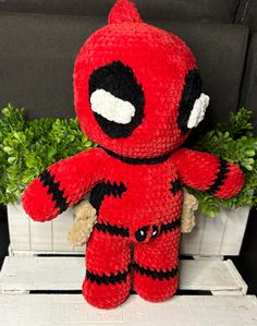 a crocheted deadpool stuffed animal sitting on top of a wooden crate next to a plant