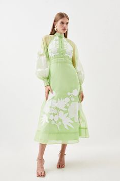 a woman is wearing a green dress with white flowers on the side and sheer sleeves