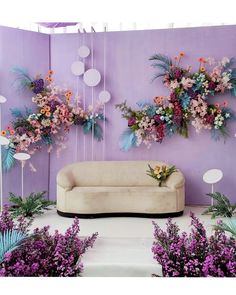 a couch sitting in front of a purple wall with flowers hanging from it's sides