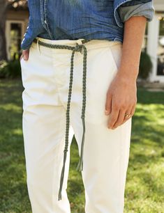 a person standing in the grass wearing white pants with a green tie around their waist