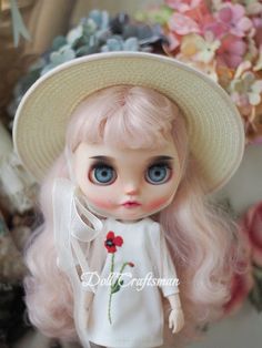 a close up of a doll wearing a hat and dress with flowers in the background