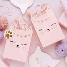 two pink bags with cats on them next to balls of yarn