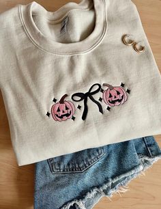 Pumpkin Bow Embroidered Sweatshirt, Coquette Halloween Sweatshirt, Fall Coquette Sweatshirt, Embroidered Halloween Sweatshirt,  Fall Embroidered Sweatshirt, Pink Halloween Sweatshirt, Spooky Season Sweatshirt Step into fall with a touch of charm and elegance with our embroidered pumpkin bow sweatshirt from the coquette collection! Made of high-quality thread, and soft fabric for maximum comfort. Sweatshirt is Gildan brand 50% cotton 50% polyester. Pictured is the sweatshirt color "sand". - Also White Custom Embroidered Top For Halloween, Cute Custom Embroidered Tops For Fall, Cute Tops With Custom Embroidery For Fall, Black T-shirt With Custom Embroidery For Fall, Black Embroidered Tops For Halloween, Halloween Embroidered Cotton Sweatshirt, Embroidered Cotton Sweatshirt For Halloween, Custom Embroidered Long Sleeve Top For Halloween, Halloween Embroidered Long Sleeve Tops