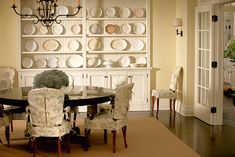 a dinning room table with chairs and plates on the wall behind it in front of a china cabinet