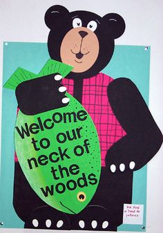 a bear holding a sign that says welcome to our neck of the woods