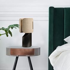 a nightstand with a lamp on top of it next to a green headboard and bed