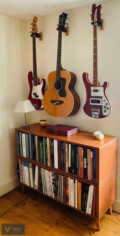 two guitars are hanging on the wall above a bookcase