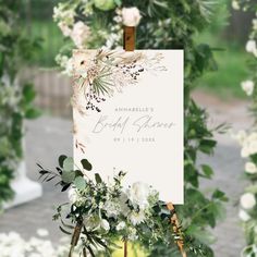 an easel with flowers and greenery on it in front of a wedding sign