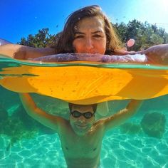 a woman under the water with a yellow surfboard on her head and another person behind her