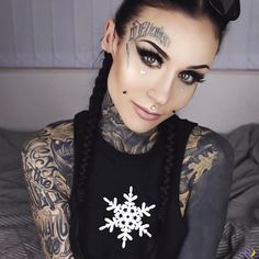 a woman with tattoos on her arm and face is sitting in bed wearing black eyeliners