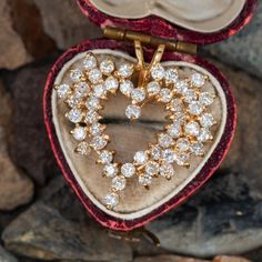 a heart shaped brooch sitting on top of a red velvet box filled with diamonds