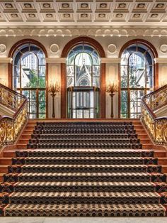 an ornate staircase leading up to the second floor in a building with large windows and chandeliers