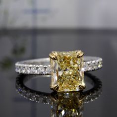 a fancy yellow diamond ring sitting on top of a black table with diamonds around it