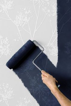 a person using a paint roller to paint a wall with blue and white flowers on it