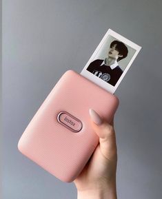 a person holding up a pink cell phone with a polaroid photo on it's side