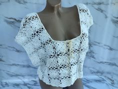 a mannequin wearing a white crochet top on a marble display case