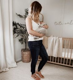 a woman standing next to a crib holding a baby in it's arms