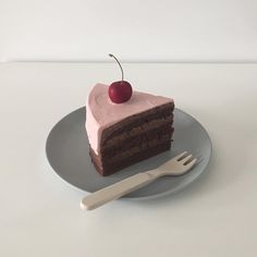 a piece of chocolate cake with pink frosting and a cherry on top, sitting on a plate next to a fork