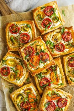 several square pieces of bread with tomatoes and cheese on them sitting on top of a piece of parchment paper