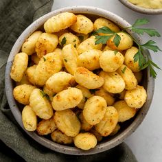 two bowls filled with cooked potatoes and garnished with parsley on the side