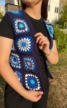 a woman wearing a blue crochet granny shawl in front of a house