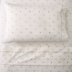 a bed with white sheets and green stars on the pillowcase, along with two pillows