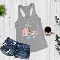 Beach Bum, Tropical Sunset and Palm Tree vintage style racerback workout or casual tank top. The model in the black tank top on the beach is 5'4'' 140lbs and is wearing a size L for a relaxed fit. Slim Fit Next Level Racerback tank-top (sizing chart in images) Material: 60% combed, ring-spun cotton, 40% polyester Extra light fabric (4 oz/yd² (135 g/m²)) Slim fit Runs slightly small since it is a slim fit. I suggest ordering one size up if you prefer a looser fit in your tank tops. Average Proces Casual Graphic Print Tank Top For Workout, Beach Racerback Top With Graphic Print, Racerback Graphic Print Top For Beach, Racerback Tops With Graphic Print For Beach, Graphic Print Racerback Tops For Beach, Sleeveless Tank Top For Beach Season Sports, Sleeveless Tank Top For Beach Sports, Sporty Racerback Tank Top For Vacation, Beach Racerback Tank Top