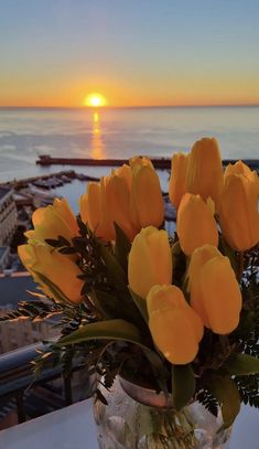 a vase filled with yellow tulips on top of a table next to the ocean