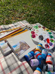 an artist's palette, watercolors and other art supplies on a picnic blanket