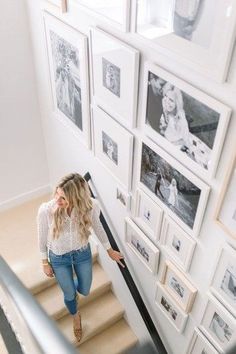 a woman is walking down the stairs in front of many framed pictures on the wall