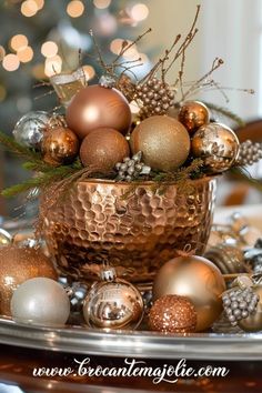 a christmas centerpiece with gold and silver ornaments in a copper bowl on a table