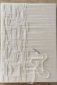 a piece of art that is made out of white paper and thread on a wooden table