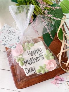 a happy mother's day cookie sitting on top of a cutting board next to flowers