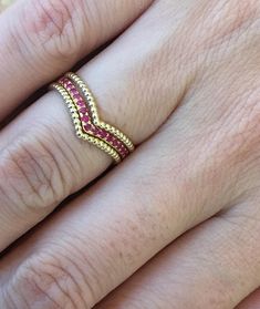 a close up of a person's hand wearing a gold ring with pink stones