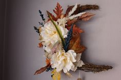 an arrangement of flowers and feathers hangs on the wall in front of a white wall