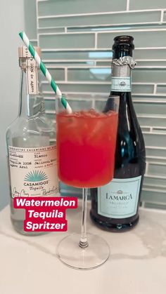 a bottle of liquor next to a glass with a straw in it on a counter