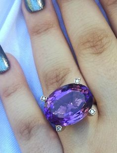 a woman's hand holding a ring with an oval shaped purple stone on it