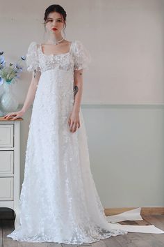 a woman in a white dress standing next to a dresser