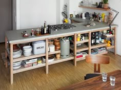 a kitchen with wooden floors and shelves filled with bottles, glasses, dishes, and utensils