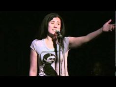 a woman standing in front of a microphone with her hand out to the side while wearing a white shirt