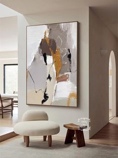 an abstract painting hangs on the wall next to a chair and footstool in a living room