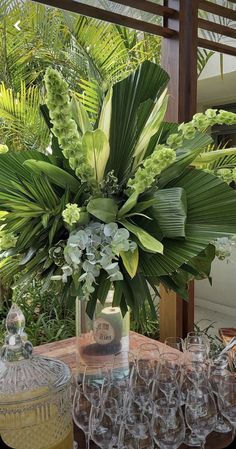 a table topped with lots of wine glasses next to a vase filled with flowers and greenery