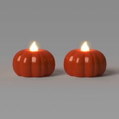 two orange pumpkin candles sitting side by side on a gray surface, with one glowing in the middle