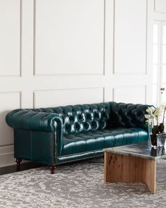 a green leather couch sitting on top of a rug next to a wooden coffee table